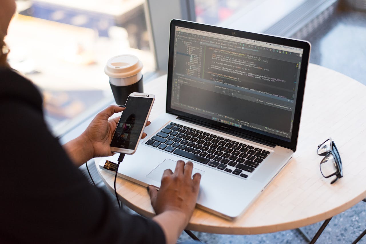 The Art of Drawing Readers In: Your attractive post title goes here Developer working remotely, coding on a laptop with phone in hand, showcasing modern work culture.